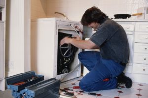 Male plumber repairing washing machine in kitchen